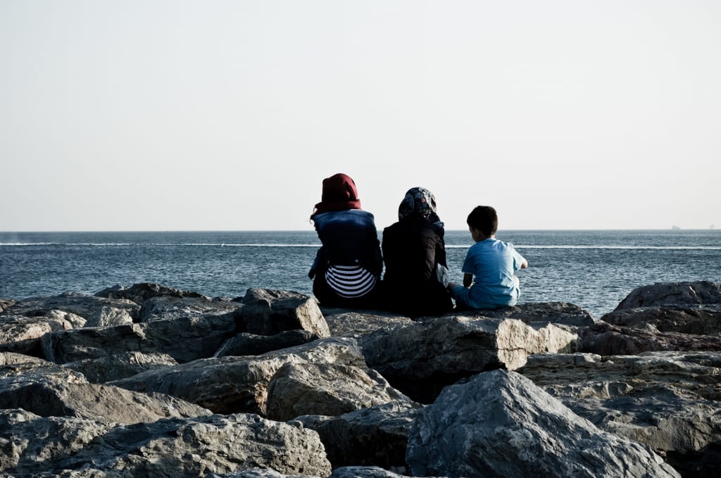 Two women and a child sitting on the rocky barrier to the Bosphorus, facing away.