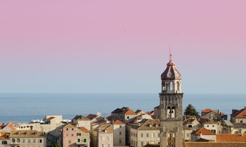 The Dubrovnik skyline with one church tower sticking up. The sky is pink at the top and blue at the bottom.