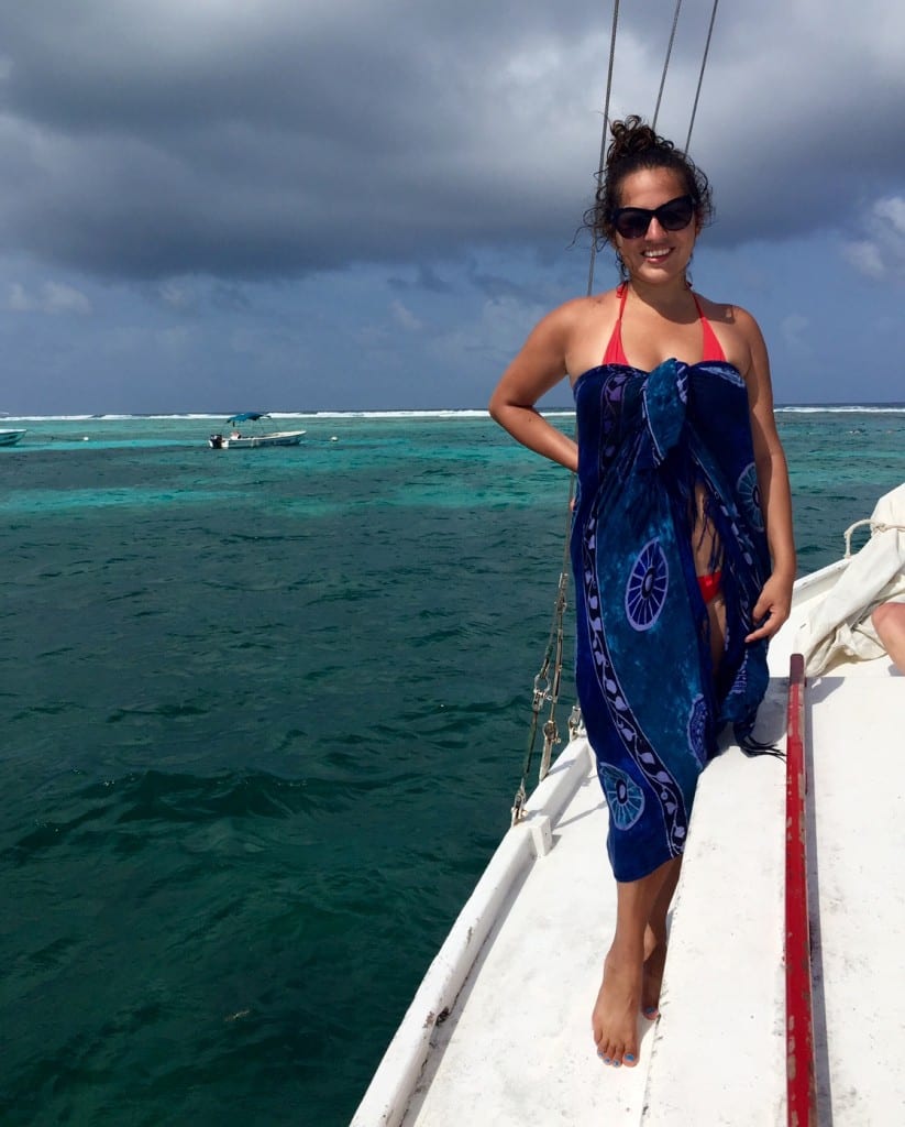 Kate stands in a sarong on a boat on top of turquoise water.