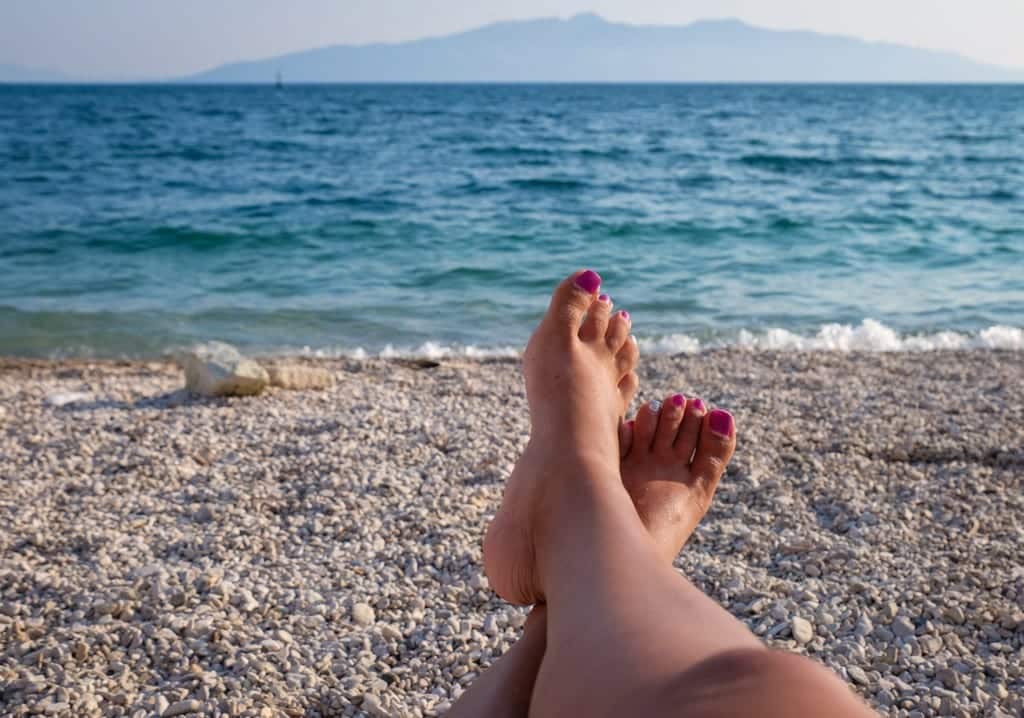 Feet on a rocky beach in front of the blue ocean, Saranda, Albania