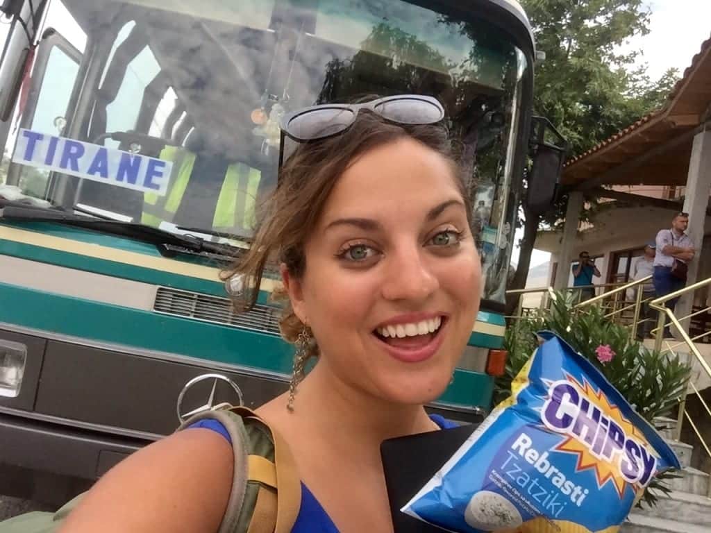 Kate stands in front of a bus bound for Tirana while holding tzatziki-flavored potato chips.