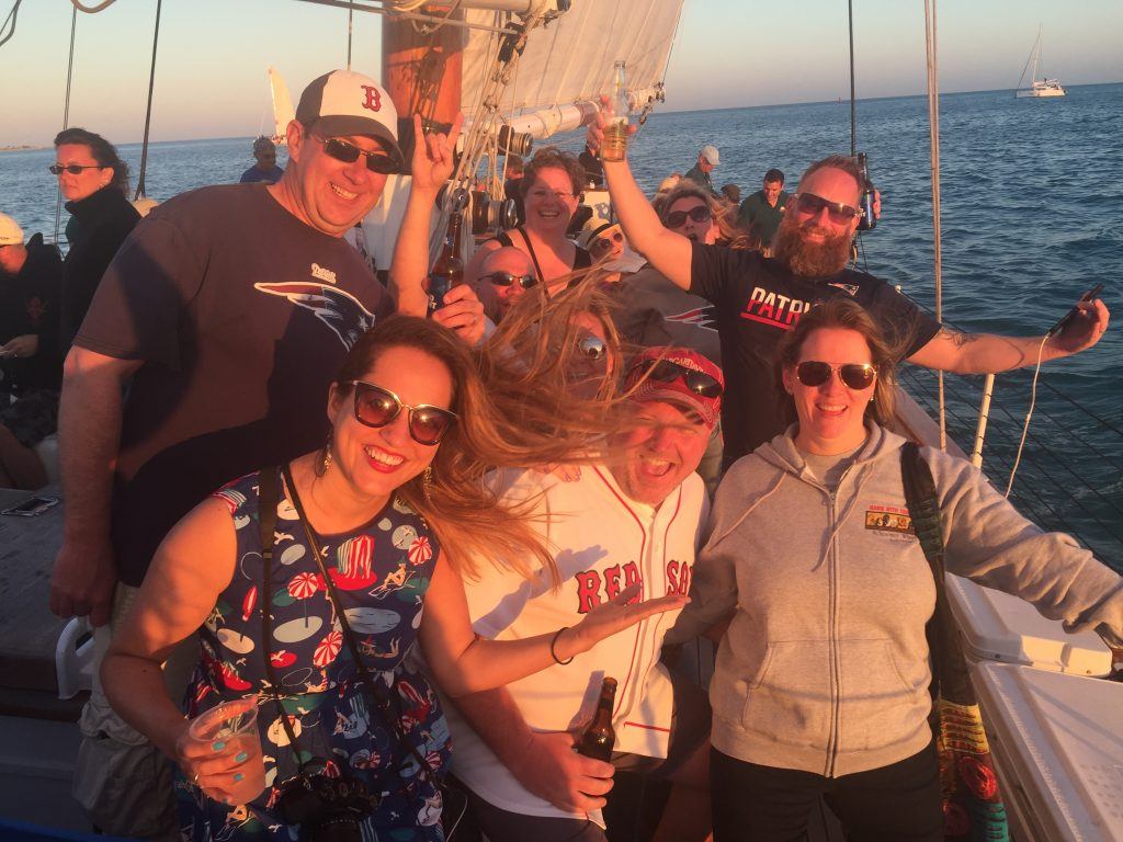 Kate and a group of 50-something folks, most of them wearing Boston sports gear, grinning in the sun on a sunset booze cruise