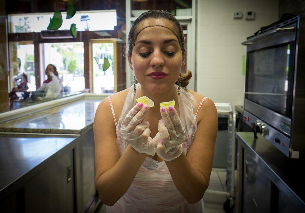 Kate in a kitchen, wearing a hair net and plastic gloves, holding two tiny key lime slices.