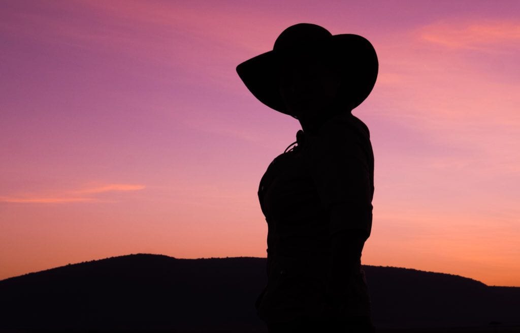 Kate silhouetted during a pink sunrise in Kenya, wearing a wide-brimmed hat.