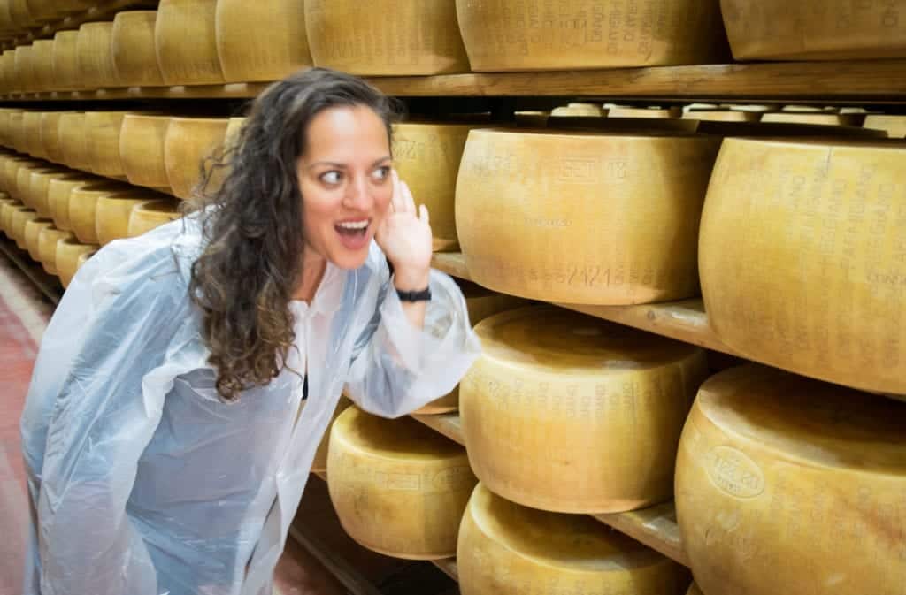 Kate leans into the rows of cheese and holds her hand to her ear like she's listening to them.