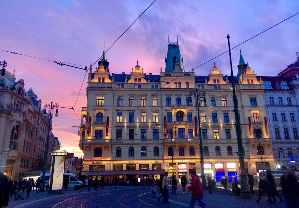 A fancy crenellated building in Prague with a bright pink and purple sunset behind it.