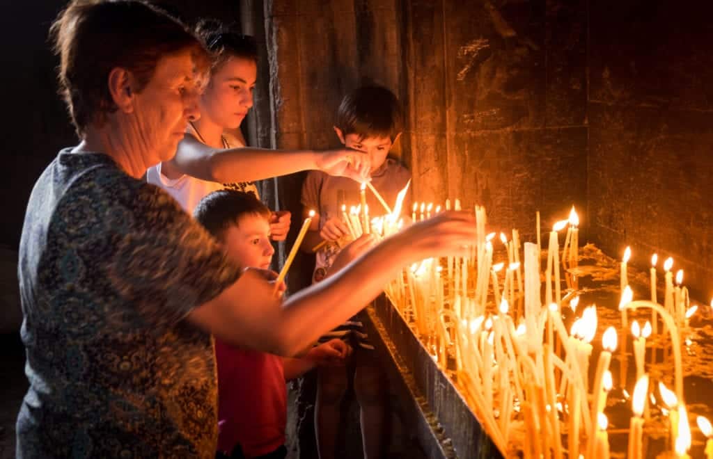 Woman and children lighting candles inside a monastery.