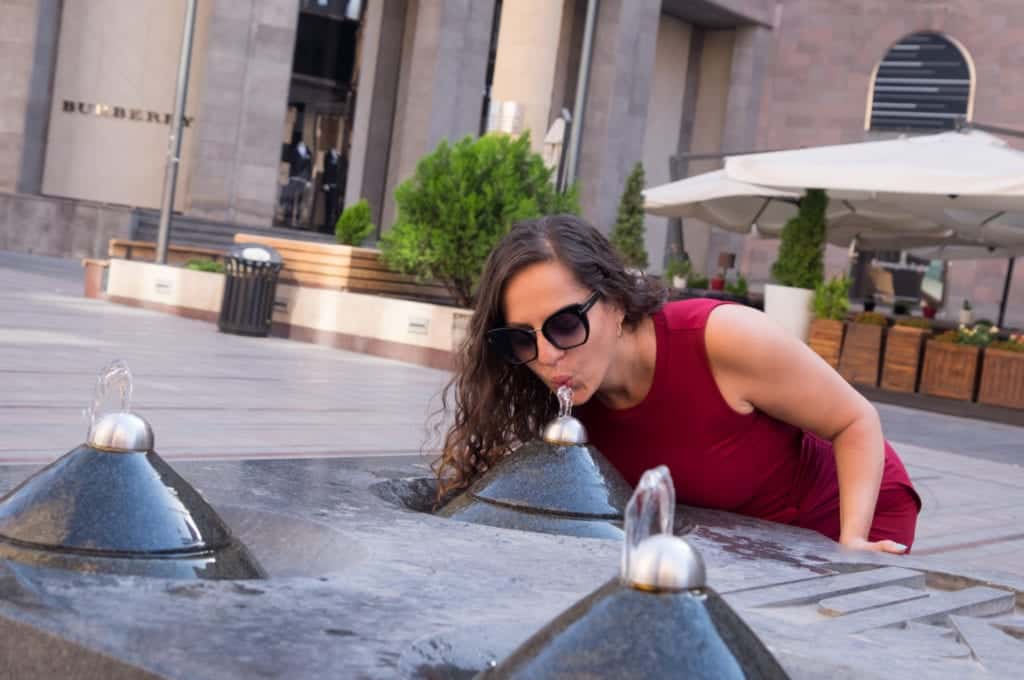 Kate leans down to drink from a pyramid-shaped water fountain in Yerevan, Armenia.