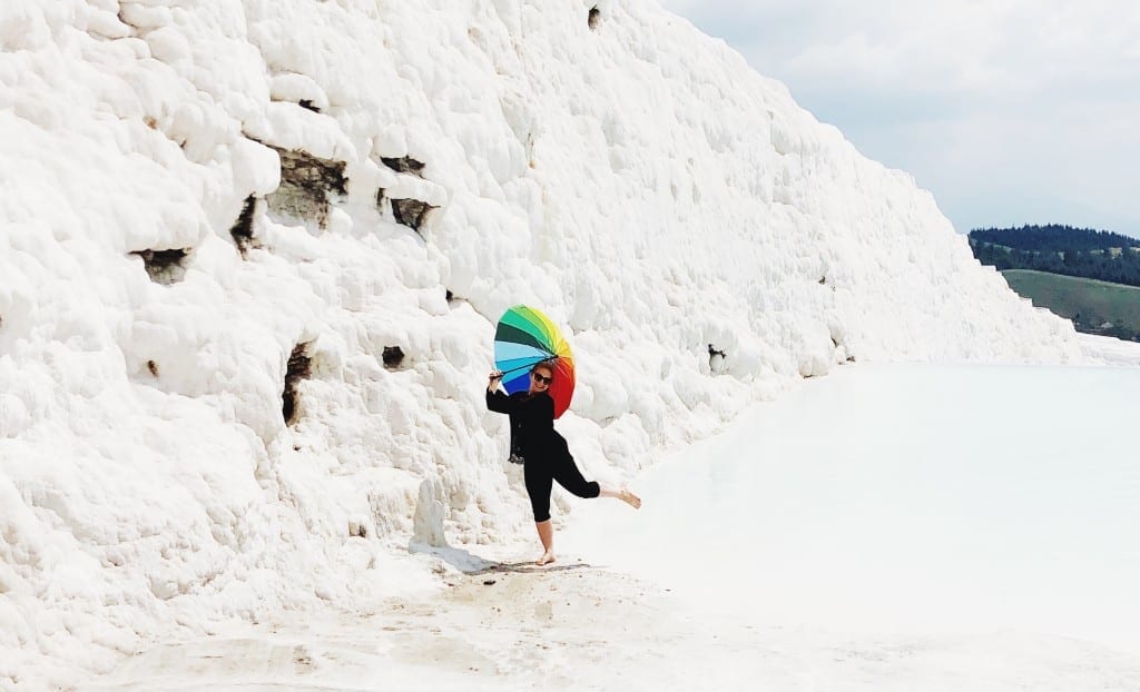 Katie dancing in the bright white travertine pools of Pamukkale, holding a rainbow-striped umbrella.