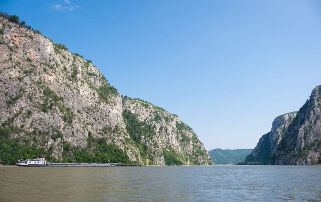 Tall limestone cliffs on the Danube and a boat with a long, flat platform for shipping goods.