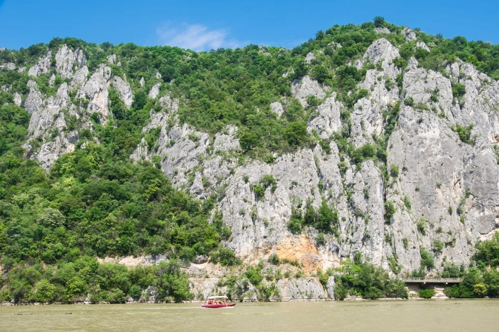 Tall limestone cliffs on the murky green Danube river, a tiny red speedboat showing you scale.