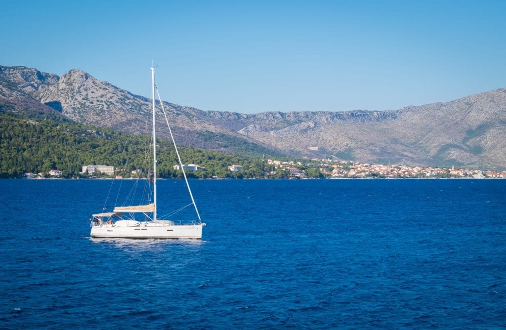 A sailboat in the navy blue water, mountains in the background.