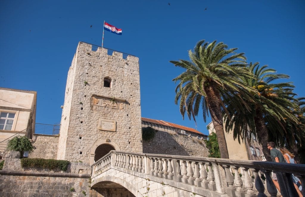A stone staircase edged with palm trees leading to a tower in Korčula's Old Town.