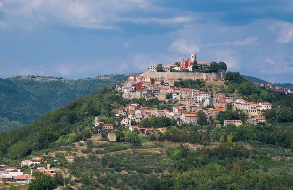 The mountaintop town of Motovun, perched on top of a hill, underneath a blue and white sky.